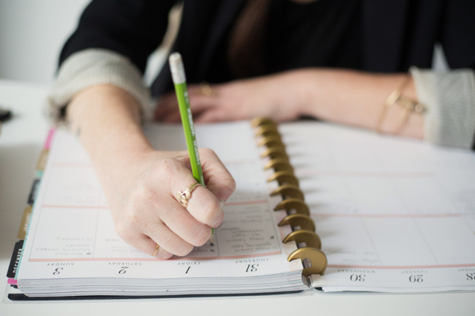 A person writing in a paper notebook at a desk